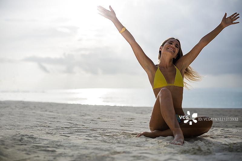 在沙滩上扬起双臂的快乐女人。图片素材