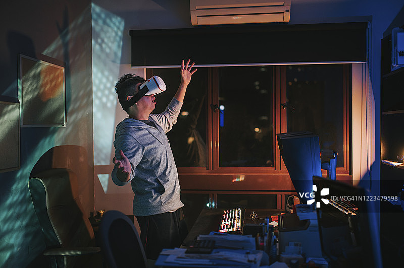 一名亚洲华人男性戴上VR眼镜，在他的家庭办公室自修室里，在他的台式电脑前体验3D虚拟游戏体验图片素材