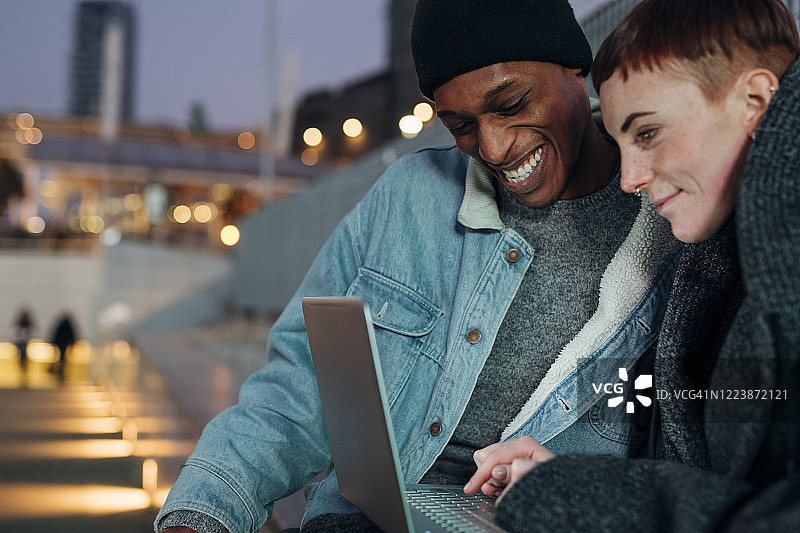快乐的年轻夫妇使用笔记本电脑在城市黄昏图片素材