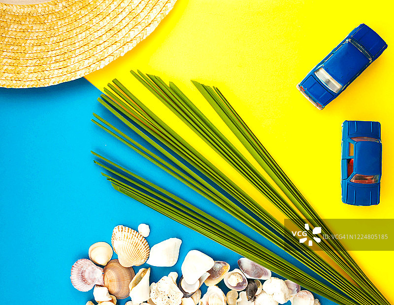夏季海滩旅游概念。棕榈树叶子，草帽，贝壳，黄色背景上的蓝色汽车图片素材