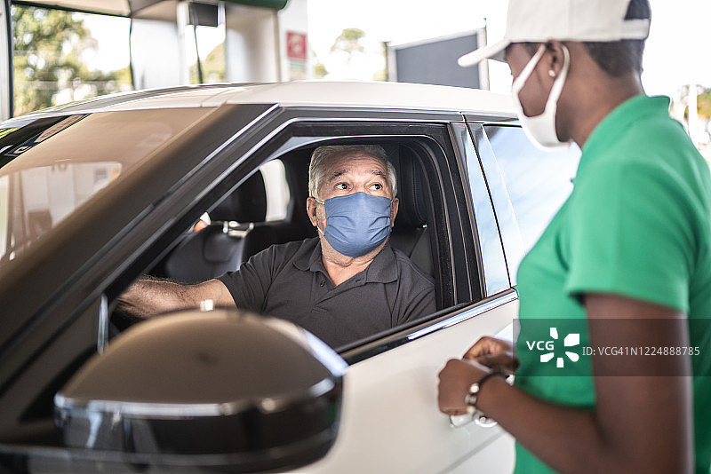 加油站服务员在加油站与顾客在汽车上交谈-戴着口罩图片素材