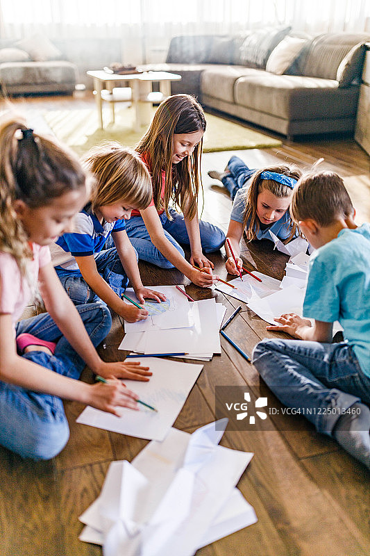 一群快乐的小朋友在家里的木地板上画画。图片素材
