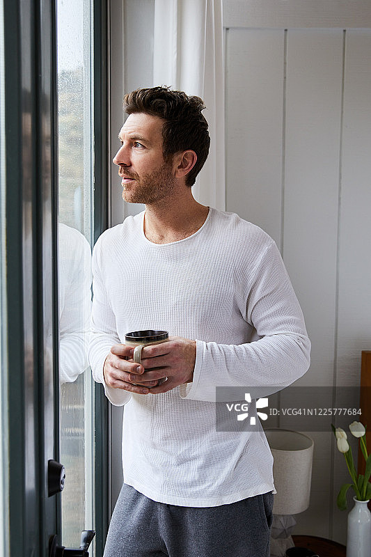 一个男人一边喝着咖啡，一边看着窗外的雨图片素材