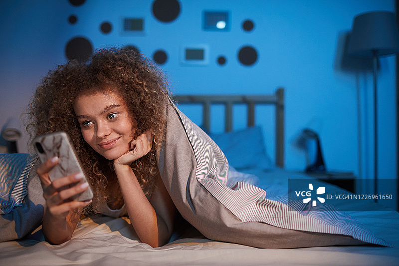 年轻女子在床上使用智能手机图片素材