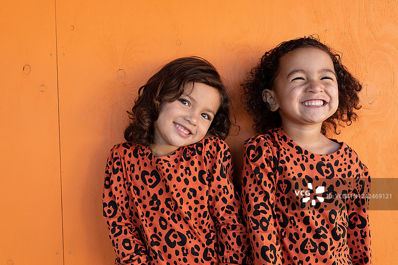 一对双胞胎姐妹站在橙色背景前笑着图片素材