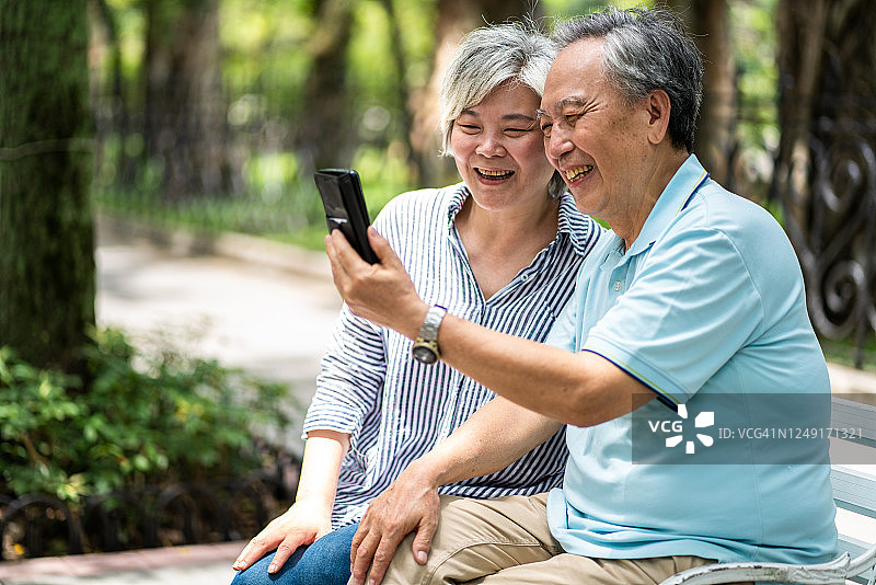 一对台湾老夫妇坐在公园长椅上用智能手机自拍图片素材