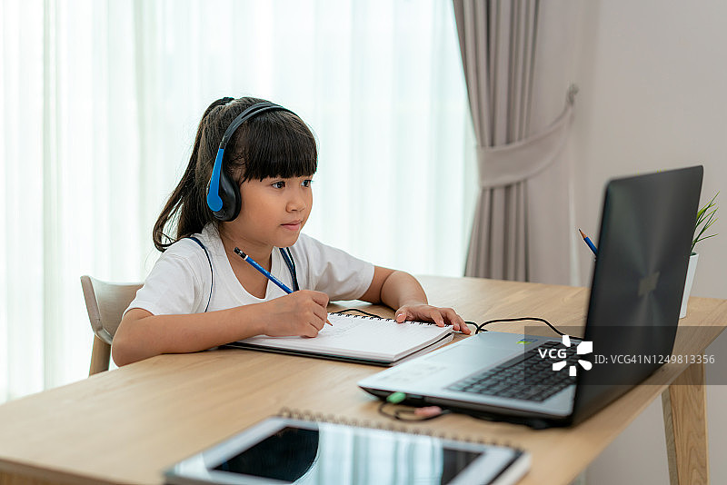 亚洲女学生视频会议电子学习与老师和同学在电脑上在家里的客厅。在家教育和远程学习，在线，教育和互联网。图片素材