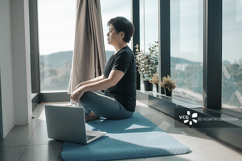 周末的早晨，一位中国美女坐在厨房靠窗的角落里的瑜伽垫上，在家锻炼身体图片素材