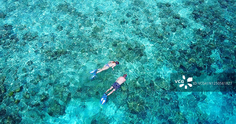 鸟瞰，俯瞰两个白人游客游泳和探索珊瑚礁在一个美丽的，阳光明媚的日子。图片素材