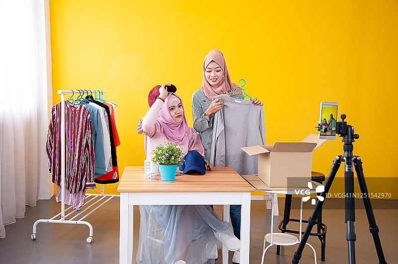 两名年轻的穆斯林妇女戴着头巾，通过视频直播在社交媒体上为她的在线时尚频道录制内容，在网上销售时尚服装。图片素材