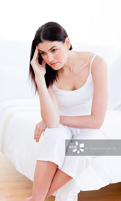 一个闷闷不乐的女人坐在床上的肖像图片素材