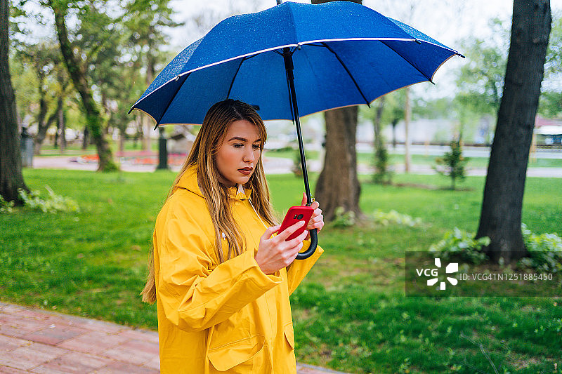 拿着蓝色雨伞用智能手机的女人图片素材