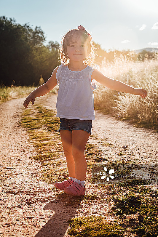 一个金发小女孩在夏天日落的泥土路上玩耍图片素材