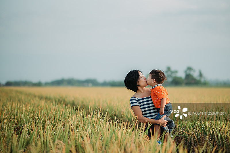 亚洲华人母亲抱着她的儿子在稻田里亲吻他图片素材