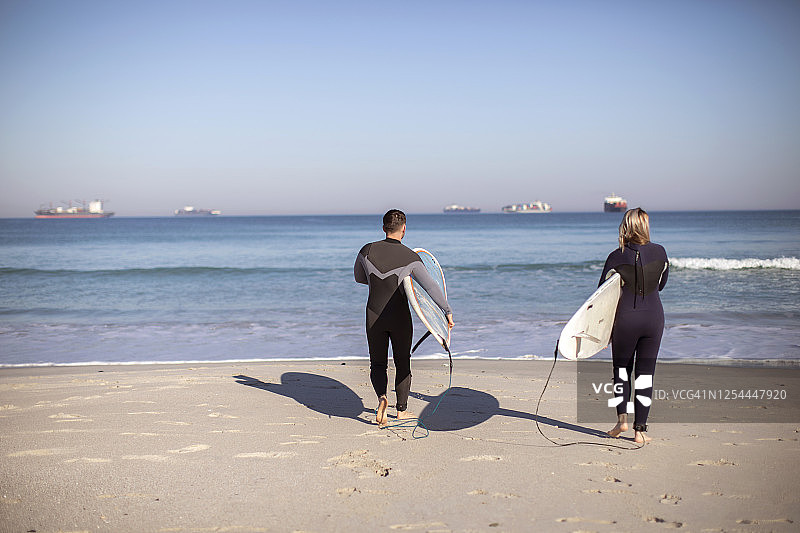 一对年轻夫妇正带着冲浪板去南非开普敦的海滩。图片素材