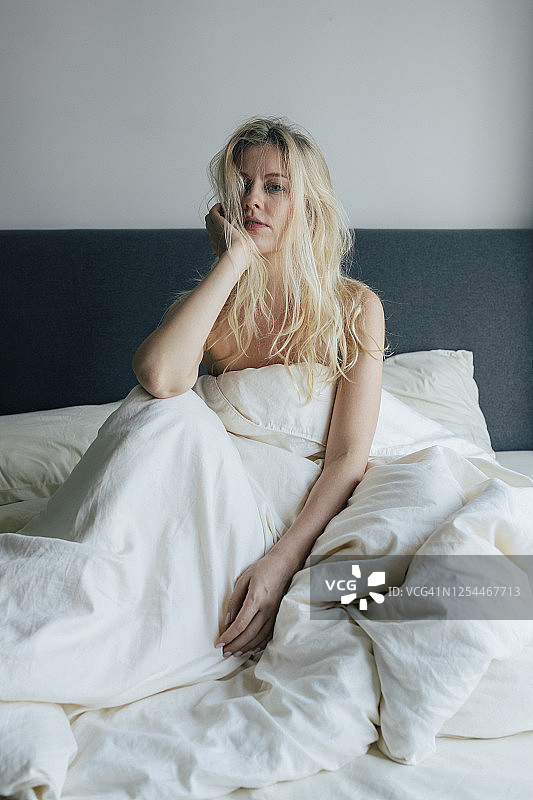 一个美丽的金发女人坐在床上，看着相机的肖像图片素材