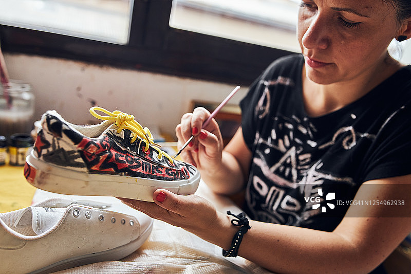 专注于创造性的女性艺术家在运动鞋上应用防水涂料图片素材