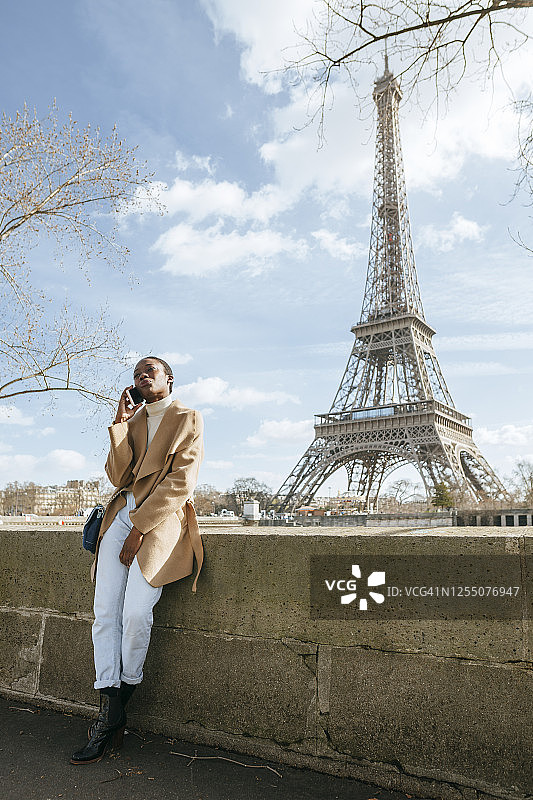 法国巴黎，一名女子站在以埃菲尔铁塔为背景的桥上玩手机图片素材