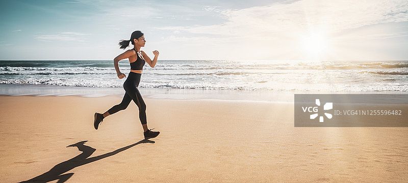日落时分在海滩上跑步的女人。一个年轻女孩的剪影沿着海滩在一个惊人的日落。图片素材