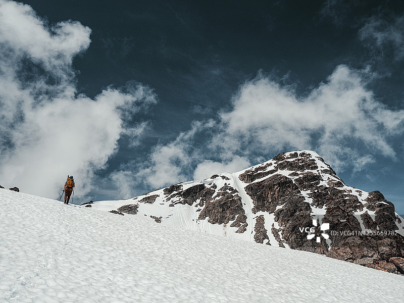 女登山者登上雪坡走向山顶，天空引人注目图片素材