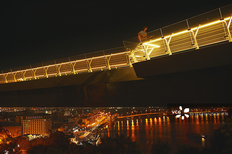 夜晚，一个人在河边的一座灯火通明的桥上弹奏着原声吉他图片素材