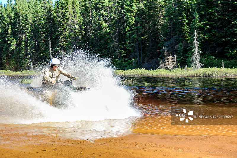 男子驾驶越野越野车高速穿过溅起水花的河水。加拿大萨德伯里的福伊湖。图片素材