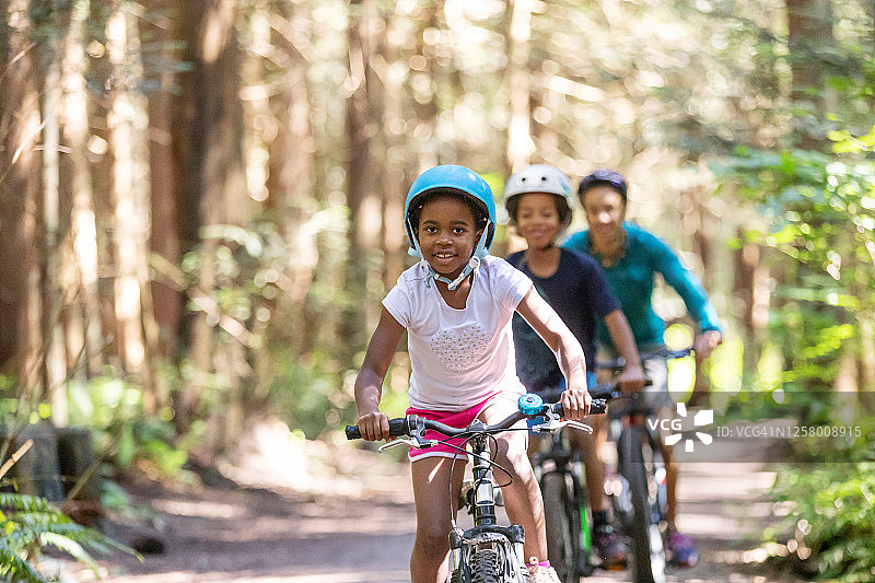 小女孩骑着自行车，哥哥和妈妈跟在后面图片素材