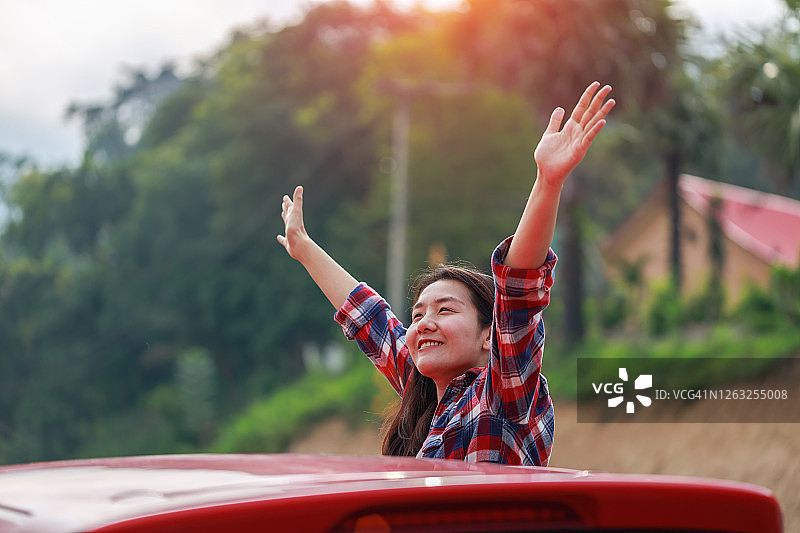 自由汽车旅行概念。一个快乐的年轻女子从车窗里伸出手图片素材