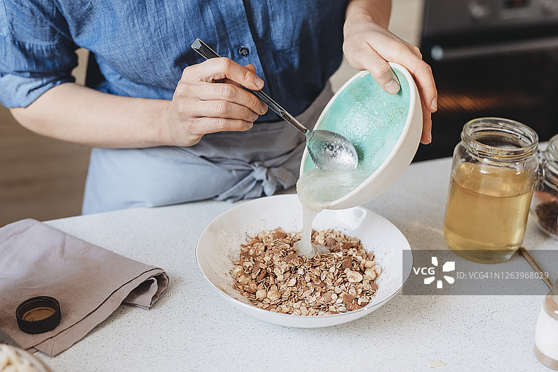 在家制作格兰诺拉麦片:一位妇女在碗中加入椰子油和燕麦和香料图片素材