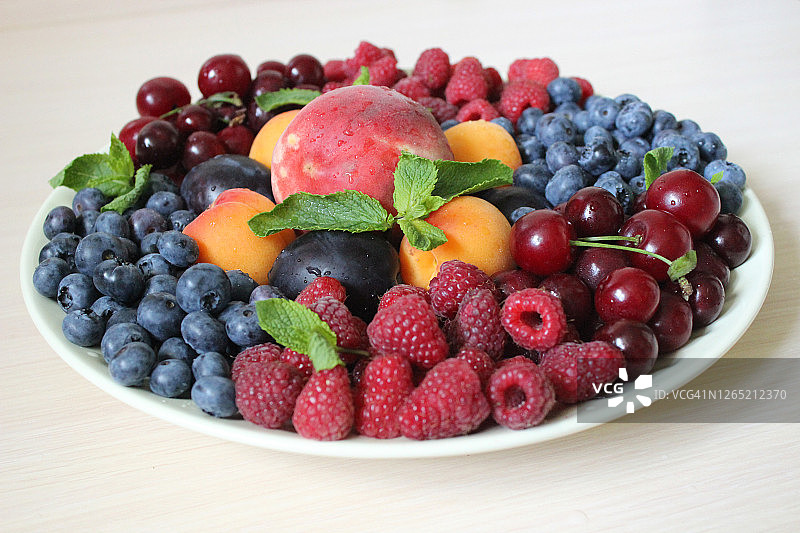 新鲜的浆果混合在白色的盘子上，在浅色的背景上。质地或背景图片素材