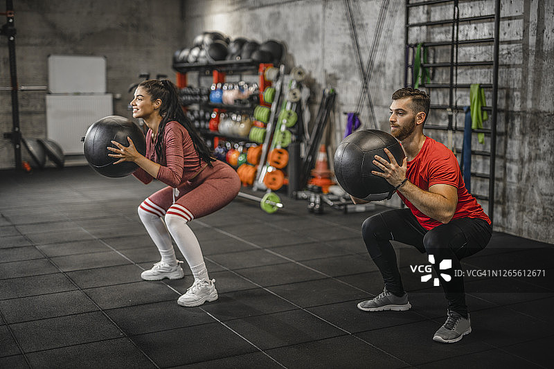 一对夫妇拿着沉重的实心球做下蹲。一名年轻男子和一名健身女子用体重球做体重练习。交叉训练时，人们蹲着举着加重球。图片素材