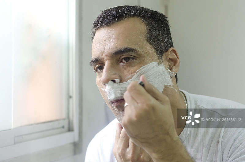 成熟的男人刮胡子，映照在镜子里图片素材