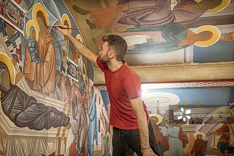 这位年轻的画家用圣徒和天使的壁画装饰东正教的墙壁图片素材