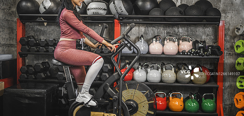 近距离的年轻健康的女人有运动训练自行车在一个健身房图片素材