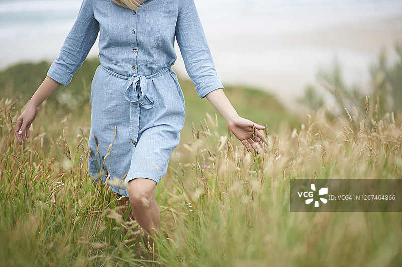 在大西洋海岸线上，一名妇女在夏日长草中行走。图片素材