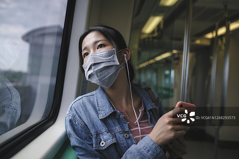 亚洲女性戴着面具，使用智能手机和耳机图片素材