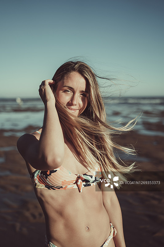微笑的年轻女子在比基尼站在大海和晴朗的天空在日落图片素材