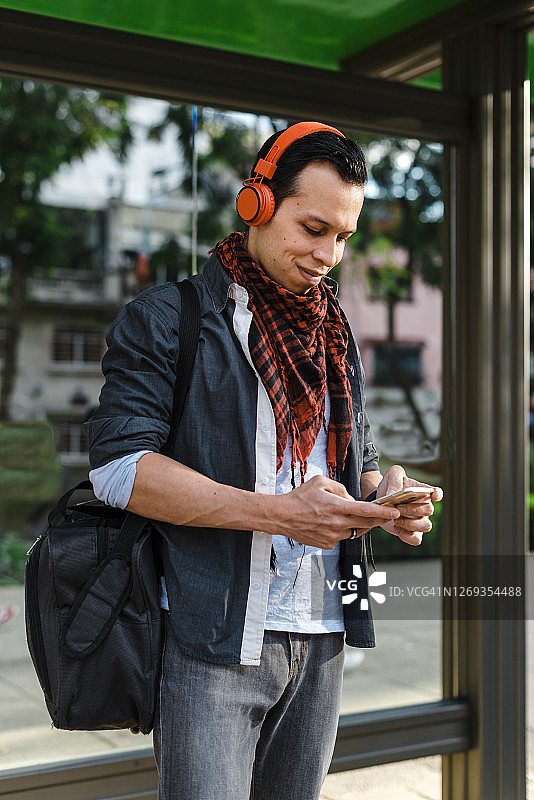 时尚达人在公交车站边用手机边耳机听音乐图片素材