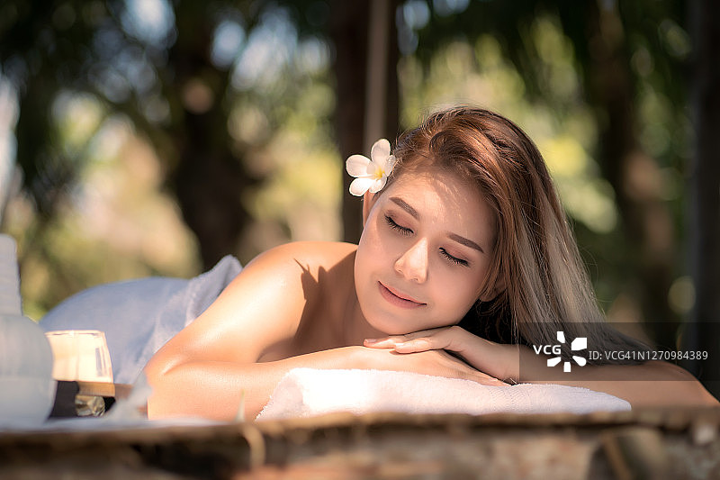 年轻美丽的亚洲女人的肖像放松按摩和温泉在木床上。图片素材