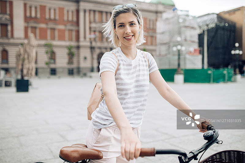 一个年轻的金发女人推着自行车沿着街道的肖像图片素材
