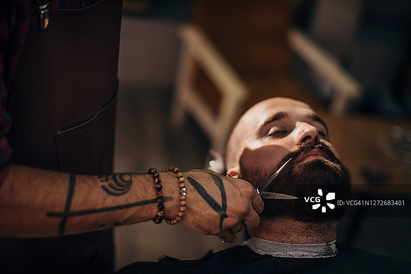 一个年轻人正在理发店里让理发师给他剪胡子图片素材