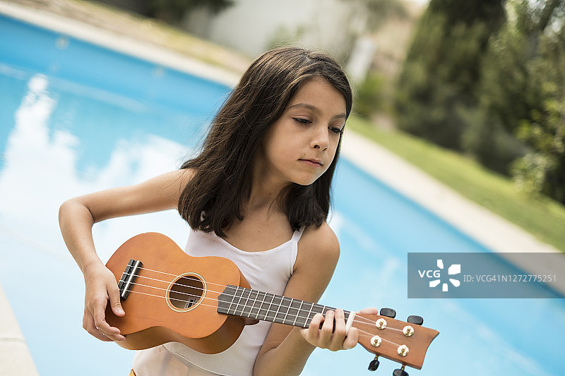 小女孩在游泳池里弹尤克里里或小吉他图片素材