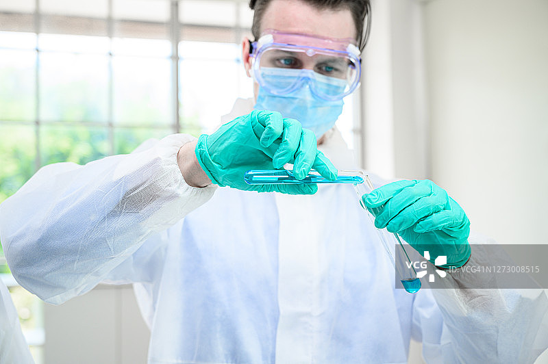 男科学家穿着防护服，拿着烧杯或管，里面装着样品液体，在实验室里使用许多实验室设备进行研究。图片素材