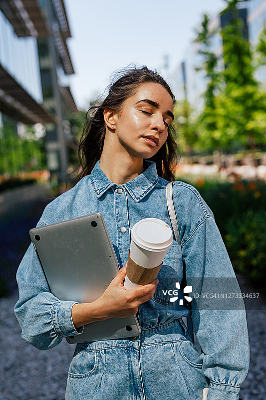 拿着外卖咖啡和笔记本电脑站在外面的女人图片素材