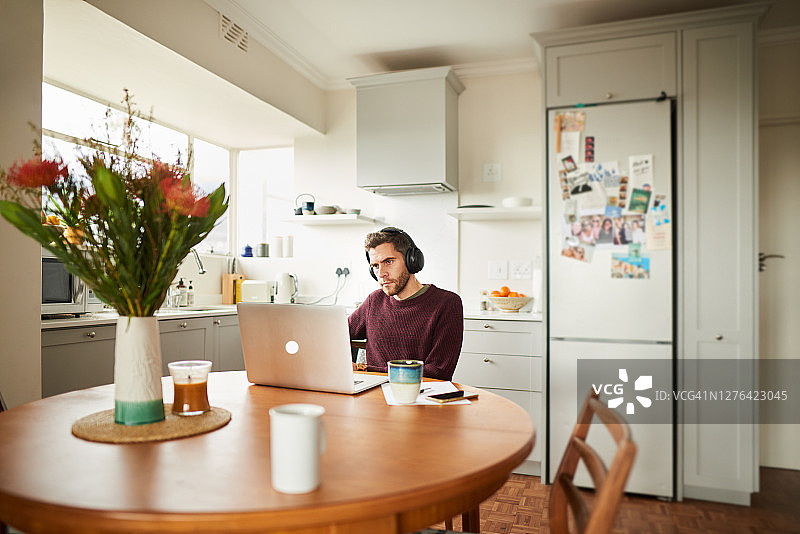 一个年轻人在厨房里用笔记本电脑远程工作图片素材