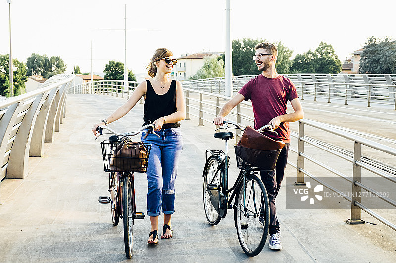 晴朗的天空下，一对快乐的夫妇在桥上骑着自行车聊天图片素材