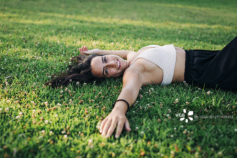 微笑的年轻女子放松在草地上的公共公园图片素材