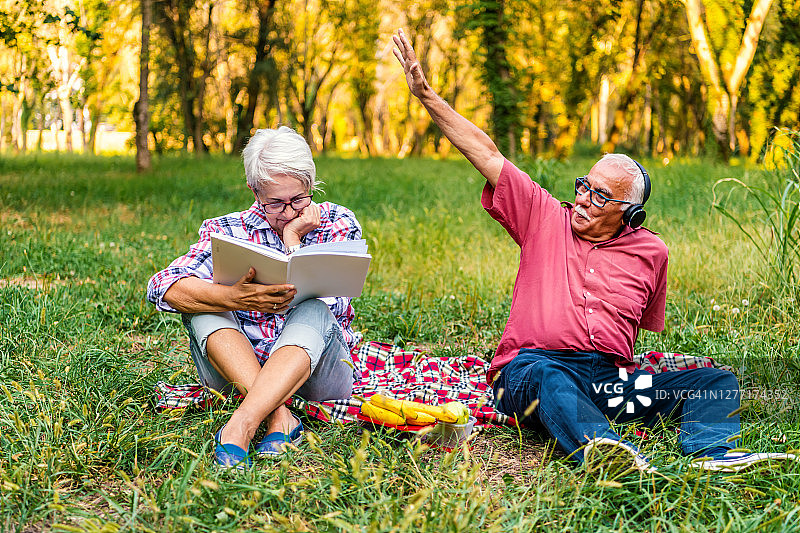 一对很棒的老夫妇正在公园里休息，一边看书，一边听音乐图片素材