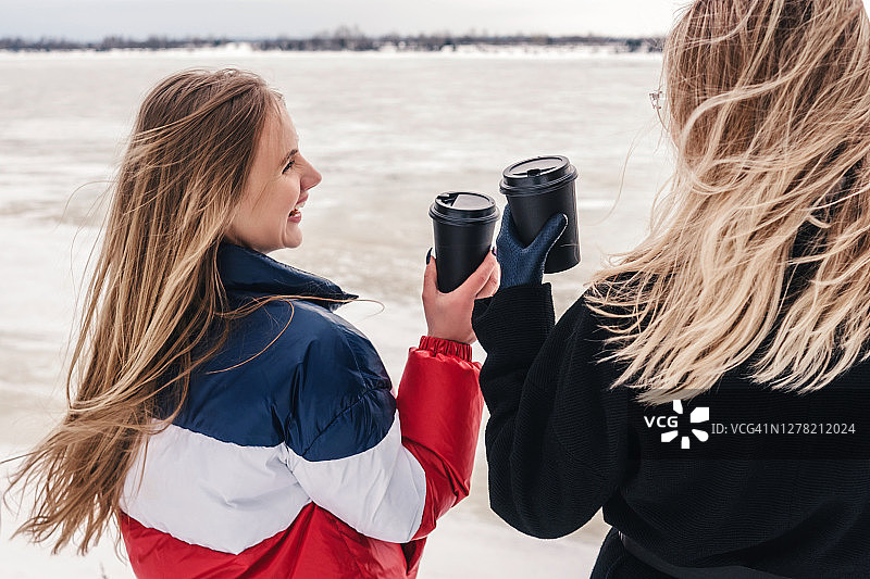 两个快乐的少女在冬天拿着咖啡杯图片素材