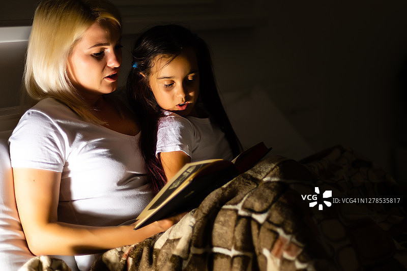 家人睡觉。妈妈和女儿在床上看书图片素材